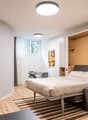 Spacious bedroom with hardwood flooring, white walls, large window, modern bed frame, built-in wardrobe, and a desk area