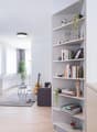 Spacious living room with white walls, hardwood floors, large windows, built-in shelving unit, potted plants, guitar, and a couch