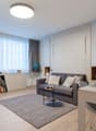 Spacious living room with large windows, grey sofa, wooden furniture, and a rug on the hardwood floor.