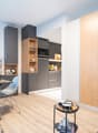 Modern kitchen with gray cabinets, wooden shelves, and built-in appliances including a dishwasher. Open concept living space with dining area and hardwood floors.