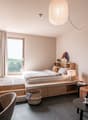 bedroom with a bed, a desk, a chair, a couch, a lamp, and a mirror, wine bottles, books on the desk