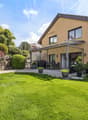 Die gedeckte Gartenterrasse lädt zum Entspannen, Geniessen und Verweilen ein. / the backyard of a home with a large green lawn in the front yard