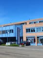 Two-story building with blue and brown exterior, multiple windows, and a parking area in front.