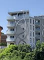 Building with modern architecture, large windows, multiple floors, white and gray facade, balconies on multiple levels, metal railings on balconies.