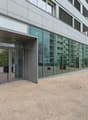 Modern office building, glass facade, entrance with glass doors, brick pavement, central location, nearby construction