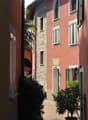 a row of brick and pink buildings, with windows and shutters, a palm tree, and a brick paved pathway