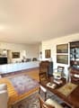 large living room with wooden dining table, 2 sofas, wooden chairs, white cupboards, wooden desk, glass cabinet, decorative items, framed pictures, carpet