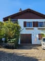 two-story house with a chimney, brown wooden exterior, wooden garage, white base