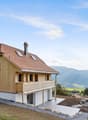 modern chalet style, wooden exterior, brown tiled roof, wooden balcony, chimney, multiple windows, raised ground
