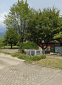paved road, grassy area, metal fence, trees, building, mountains in the background