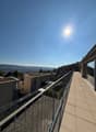 The building has a balcony with a metal railing and tiled flooring. From the balcony, there is a view of the city with many buildings and greenery.