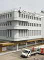 multi-story office building, white exterior, glass windows, red sign reading 'KOPFLI PARTNERS', multiple parked vehicles in the front
