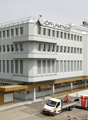 multi-story office building, white exterior, glass windows, red sign reading 'KOPFLI PARTNERS', multiple parked vehicles in the front