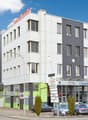 5 story building, large glass windows, green accents, garage entrance, cars parked in front