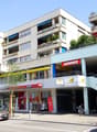 Multi-story commercial and residential building with balconies, parking spaces, and various retail stores on the ground floor including Denner supermarket.