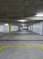 Large indoor parking garage with concrete floors, yellow painted lines and columns, and white tiled walls.