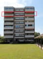 Apartment building, multiple balconies, brick exterior, two floors, surrounded by a landscaped lawn