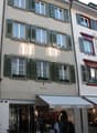 3 story building, white walls, green shutters, red trim, multiple windows, shops on the ground floor
