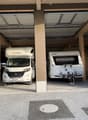 Two vehicles parked in a garage, one is a camper van and the other is a trailer.