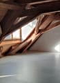 Spacious attic with exposed wooden beams and trusses, large windows providing natural light, concrete floor, and potential for conversion or storage space.
