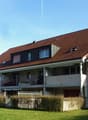 3 story residential building, brown roof, balconies on 2nd and 3rd floor, fence, grass