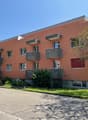 3-story apartment building, orange exterior, multiple balconies, windows, concrete base, greenery