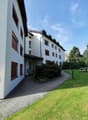 White multistory building with red windows, brick pathway, green grass, bush, bench