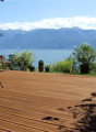 Wooden deck, outdoor table, outdoor chair, multiple potted plants, view of a lake and mountains