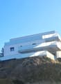 Modern design multistory house with glass balconies and terraces, white exterior, yellow walls, situated on a hill