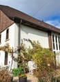 two-story house, brown roof, white wall, several windows, multiple potted plants, white lawn umbrella, greenery