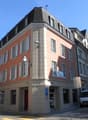 5-story building, red brick, white shutters, several windows, lamp on wall, multiple vans parked