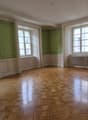 room with wooden floor, green walls, 3 windows, radiators on both sides, mirror on right wall, pictures hanging on the wall