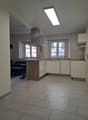 Modern kitchen with island, white cabinets, central island, sink with faucet, kitchen windows, tiled floor, overhead lighting.