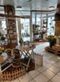 Room filled with decorative items and floral arrangements, white tiled flooring, wooden tables and benches, natural light from windows
