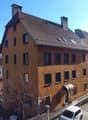 3 story house, brown roof, multiple windows, cars parked on street