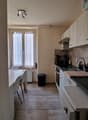 kitchen with dining area, white walls, wooden floor, white cabinets, white dining table, white chairs, white washing machine, dishwasher, white radiator, windows with white curtains, trash bin, ceiling lights