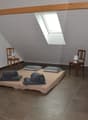 Attic bedroom with slanted ceiling, large window, hardwood floors, wooden beams, and a bed with gray bedding