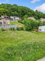 The image shows a residential area with several multi-story houses and apartments nestled in a lush, green landscape. The buildings have balconies and terraces, and the surrounding area is covered in grass and trees. The scene appears to be in a suburban