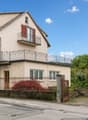 2 story house, beige exterior, red shutters, iron railing on balcony, wooden front door, garage at side, black gate