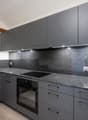 Modern kitchen with grey cabinets, granite countertops, built-in oven, induction cooktop, and modern fixtures.