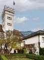 Large white house with tower, flag, red roof, garden, mountains in the background