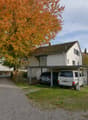 Single-family house, covered carport with two cars, tree in front, gravel driveway