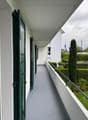 balcony with green shutters, gray floor, white walls, green railing, view of a garden