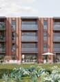 4-story modern apartment building with red brick facade, large windows, and balconies. The building is surrounded by a well-maintained garden with various flowering plants and shrubs.