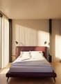 A bedroom with a large bed, white walls, wooden floor, large windows with white curtains, and two wall lamps