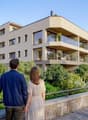 Modern apartment building, multiple floors, glass balconies, brick wall, greenery