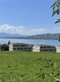 Wide field of grass, overlooking a large lake, multiple apartment buildings, mountains