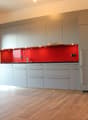 Modern kitchen with gray cabinets, red backsplash, stainless steel faucet, black oven, and wooden floors.