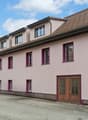 pink facade, brown roof, multiple windows, ground floor entrance, parking area, balcony