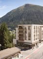 modern apartment building in a mountainous area with several houses, mountains, and greenery